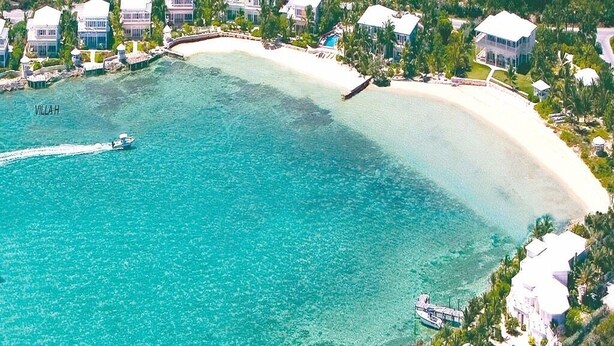Ein Luftbild eines Küstenresorts mit mehreren Villen, einem klaren türkisfarbenen Meer und einem Bootssteg.