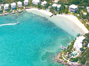 Vue aérienne d’une station balnéaire comprenant plusieurs villas, une mer turquoise aux eaux limpides et un quai pour bateaux.