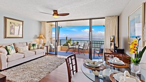 A spacious living room with a balcony, a dining area with a glass table, and a view of the ocean. - Open, spacious 1bd  with oceanfront views (Lahaina)