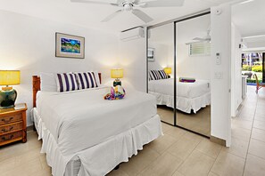 Habitación de hotel con una cama grande, dos mesitas de noche con lámparas, un ventilador de techo, un espejo grande y vistas al exterior.