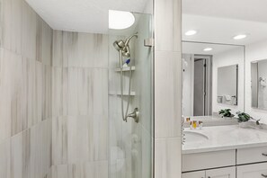 Un baño moderno con ducha envuelta en vidrio, tocador de mármol blanco y un espejo grande.