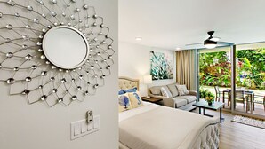 A modern hotel room with a large bed, a seating area with a sofa and chairs, a dining table, and a balcony with a view of greenery.
