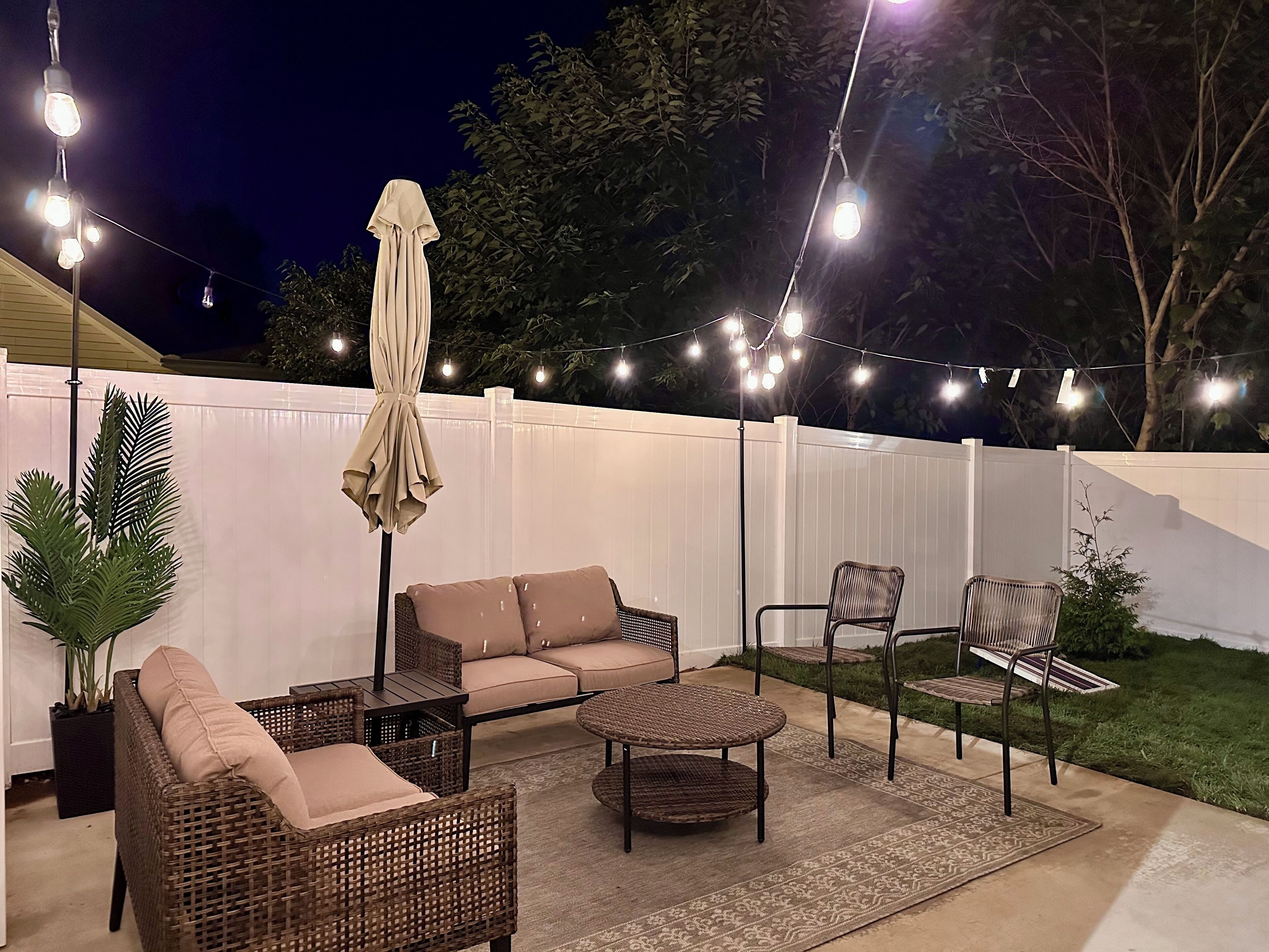 Un espace extérieur aménagé en terrasse, avec des meubles en osier, une table à manger et des guirlandes lumineuses.