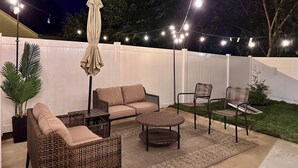 An outdoor patio area with wicker furniture, a dining table, and string lights.
