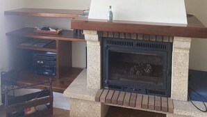 Una chimenea con revestimiento de piedra y una repisa de madera, un cuadro en la pared y un pequeño florero sobre la repisa.