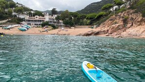 Un kayak en aguas tranquilas, con una playa y edificios al fondo.