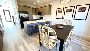 A modern kitchen with a central island, bar stools, and a dining table with chairs. - Trendy 5 BD/4.5 BA St. George Townhome at The Vue (St. George)