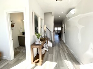 Stunning hallway with a console table, potted plant, and artwork, leading to a staircase with a glass railing.