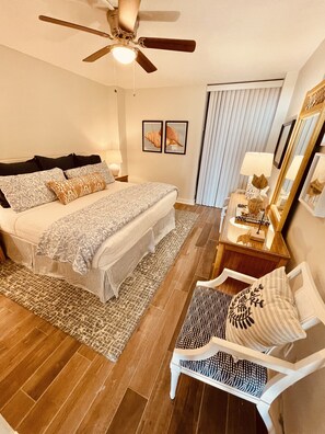 Une chambre à coucher comprenant un lit, des tables de chevet, une chaise, un ventilateur de plafond et un miroir.