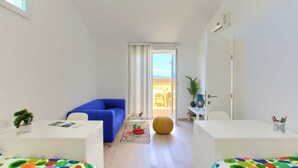 Ein moderner, gut beleuchteter Raum mit einem blauen Sofa, einem kleinen Tisch mit einer Pflanze und einem farbenfrohen Teppich.
