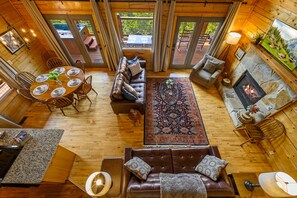 A cozy cabin interior with a dining area, a fireplace, and a living room with a large rug and leather sofa.