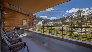 Un balcón con sillas de madera, una parrilla y vistas a un paisaje montañoso.