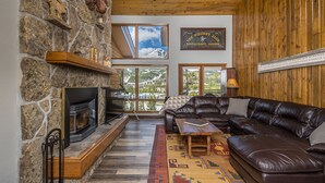 Una sala de estar acogedora con una pared de piedra, una chimenea, un sofá de cuero y vistas a una montaña nevada.