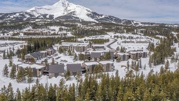 Un complejo turístico cubierto de nieve con varias edificaciones, una pista de esquí y una montaña al fondo.