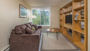 Ein Wohnzimmer mit einem braunen Sofa, einem kleinen Couchtisch und einem Holzregal.