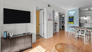 Een moderne woonkamer met een flatscreen televisie, een donker houten kast en een eethoek met een tafel en stoelen.