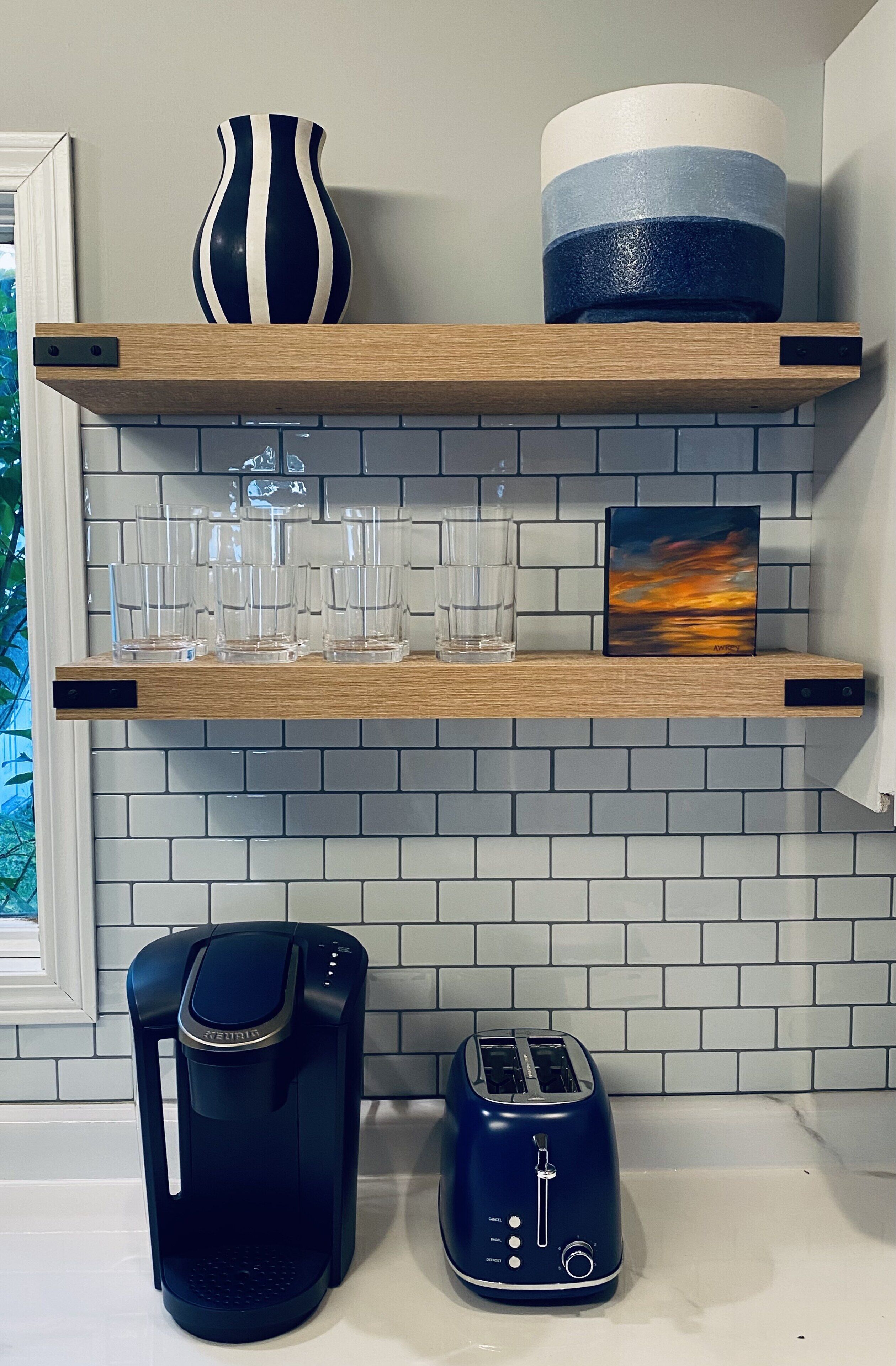 A kitchen with a coffee maker, toaster, and a shelf with glasses and a vase.
