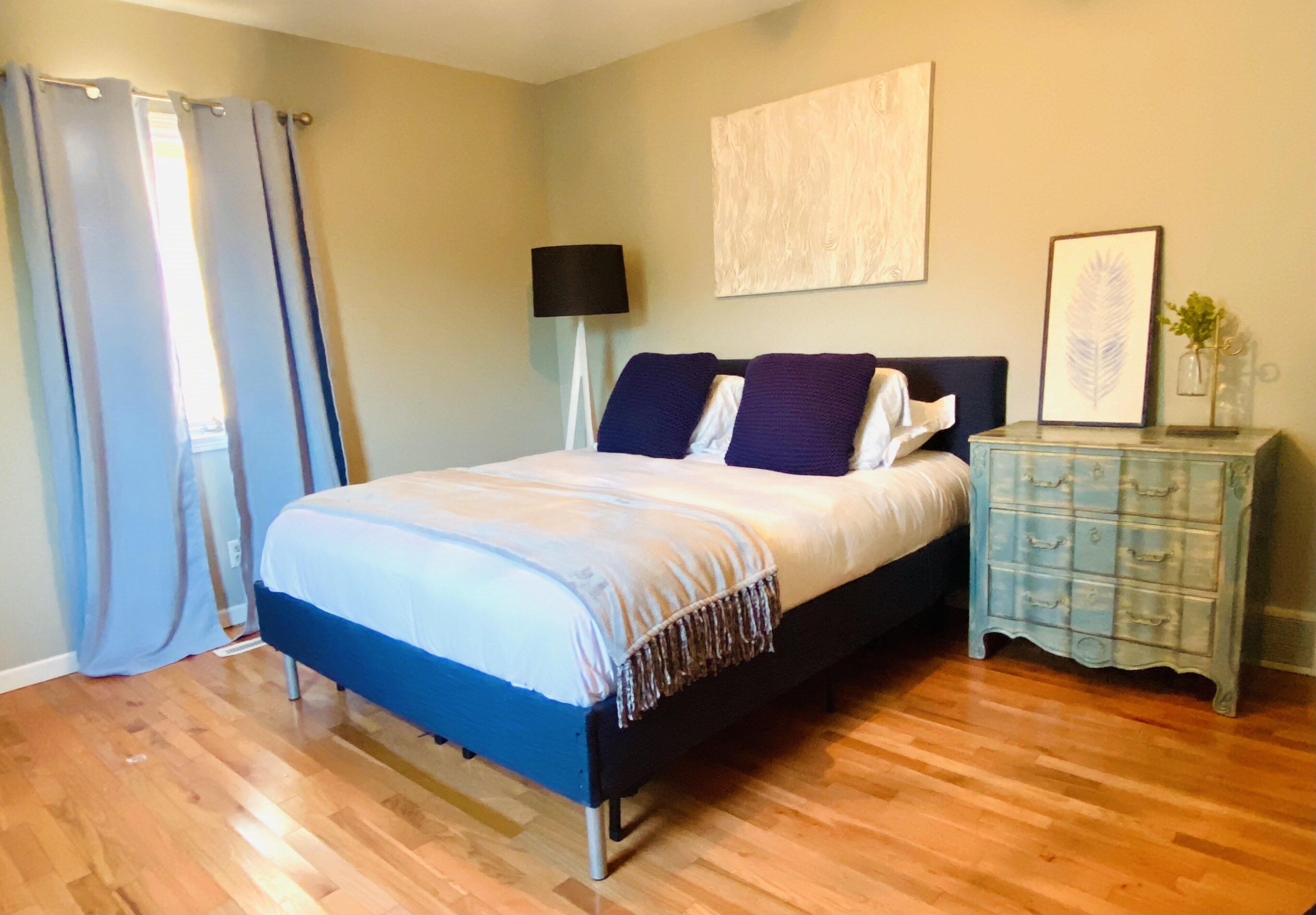 A bedroom with a bed, a dresser, a lamp, and a painting on the wall.