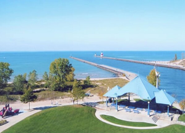 Un parc côtier doté d’une jetée qui s’avance dans la mer, d’une zone herbeuse avec un pavillon au toit bleu, et d’un ciel d’un bleu limpide.