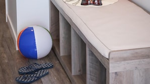 Un banc avec un coussin, un ballon de plage et des tongs sur le sol.