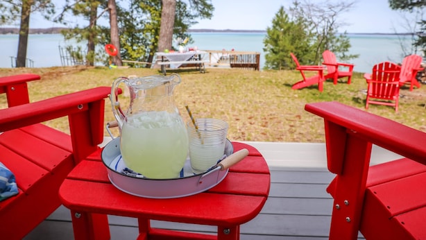 Une table rouge avec une carafe de limonade et des verres, placée sur une terrasse donnant sur un lac.