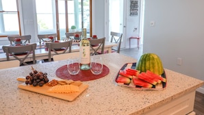 Une cuisine avec une table à manger dressée pour quatre personnes, un comptoir sur lequel on trouve une bouteille, des verres et une pastèque.