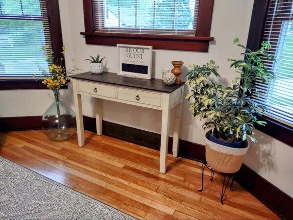 Un escritorio de madera con un cartel en marco, un jarrón con flores y una planta en maceta.