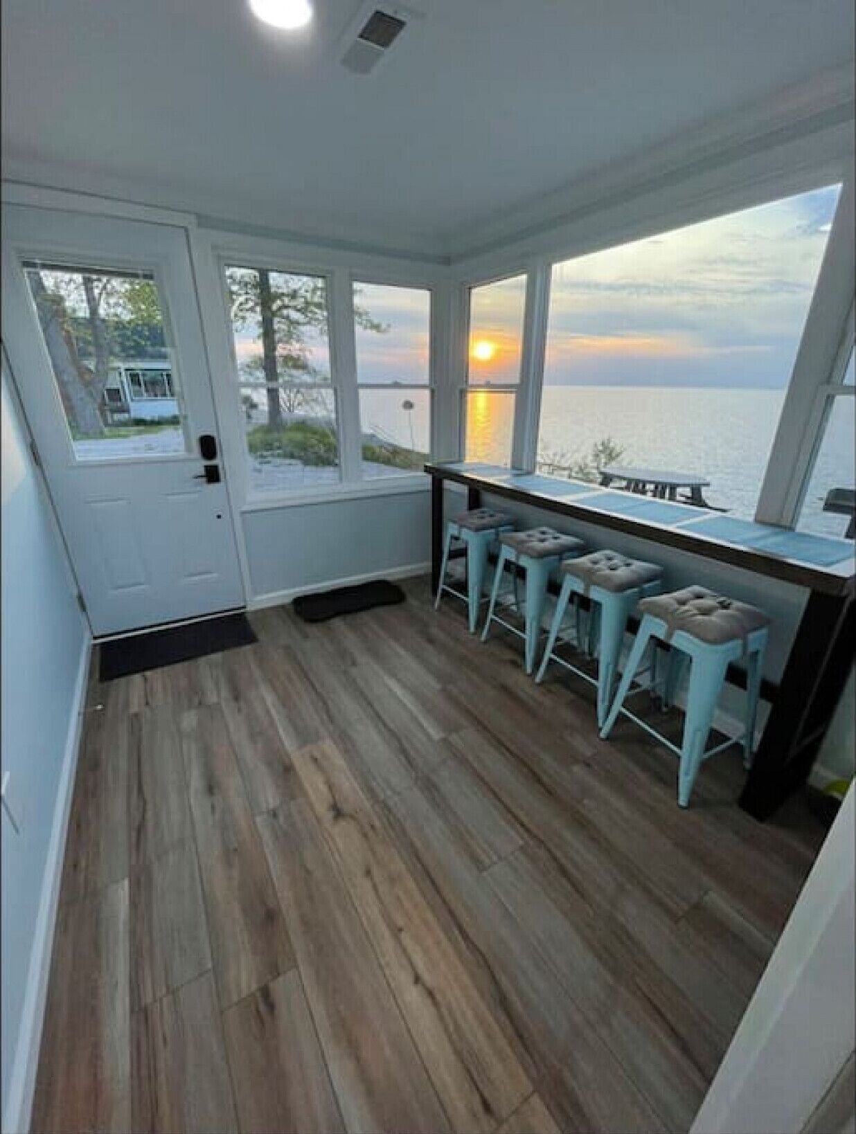 A room with a wooden floor, a door, and a view of the sunset over the water.