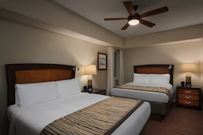 Two single beds with bedside tables and lamps, a ceiling fan, and a window with curtains.