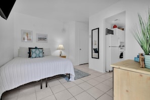 A bedroom with a bed, bedside table, lamp, and a small desk with a mirror and items on it. - #4286 PB Studio Walk to BAY, PIER & BEACH 🏝 (San Diego)