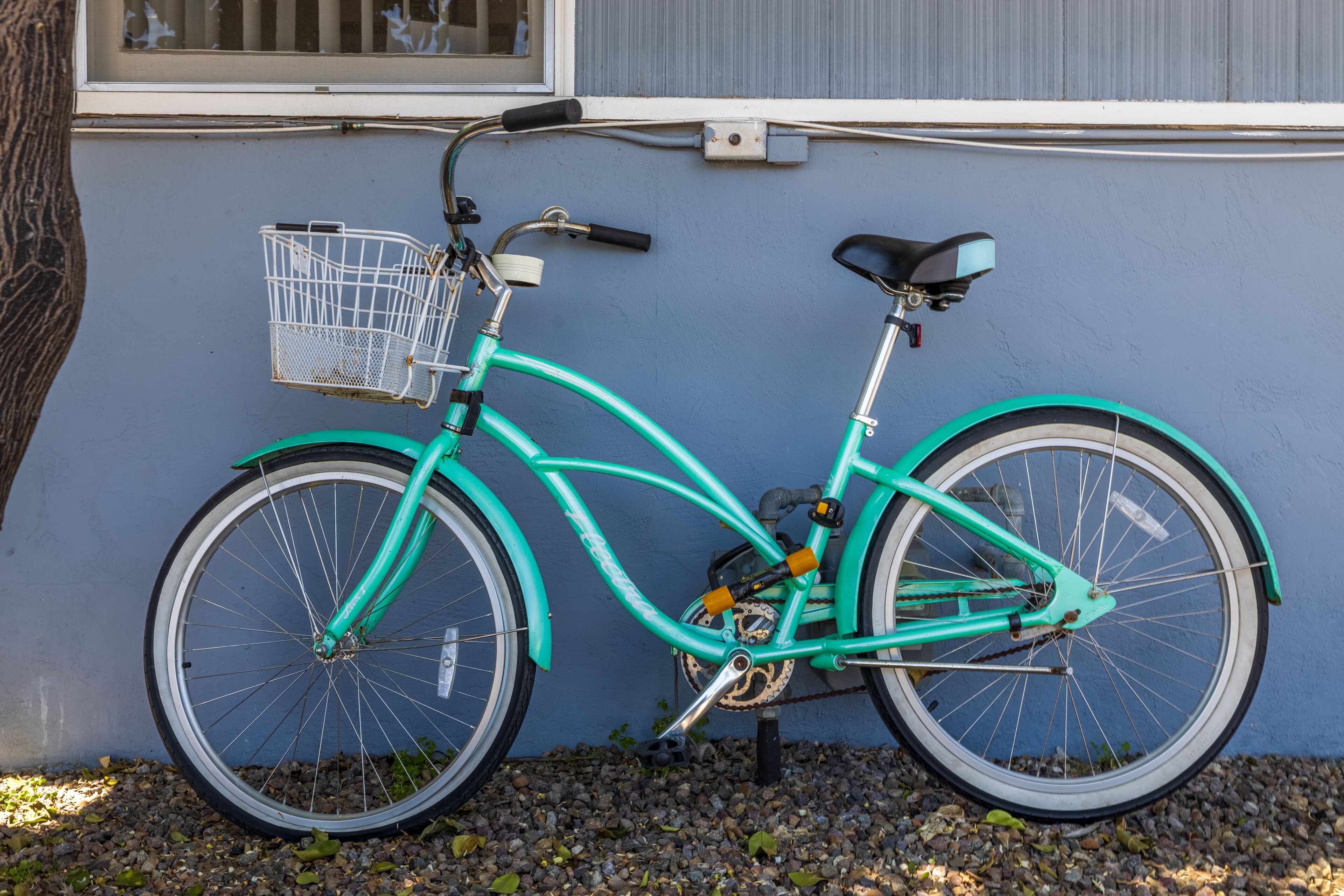 A teal bicycle parked against a wall with a basket attached to the front.