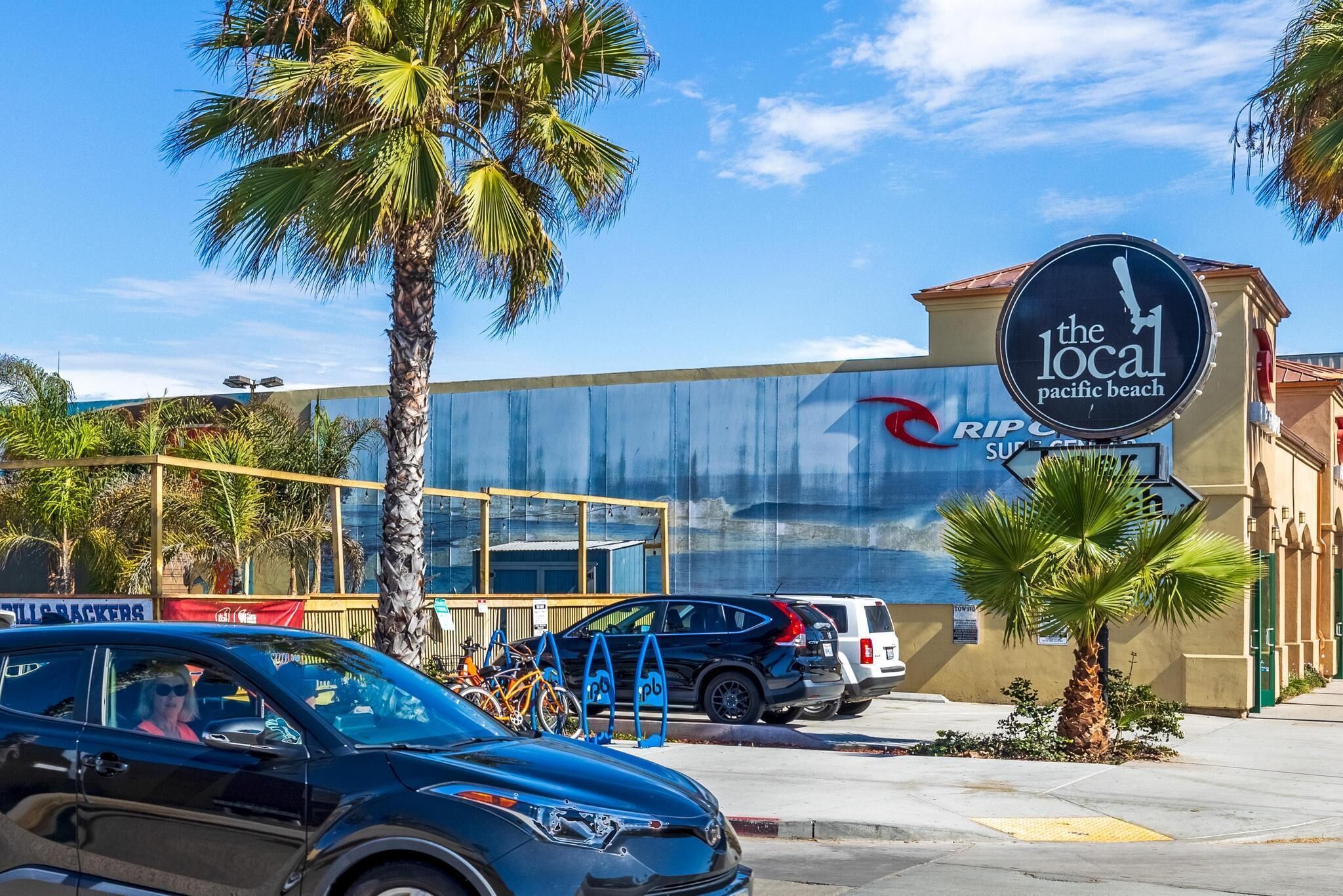 Un edificio con un letrero que dice 'The Local Pacific Beach' y un estacionamiento con bicicletas.