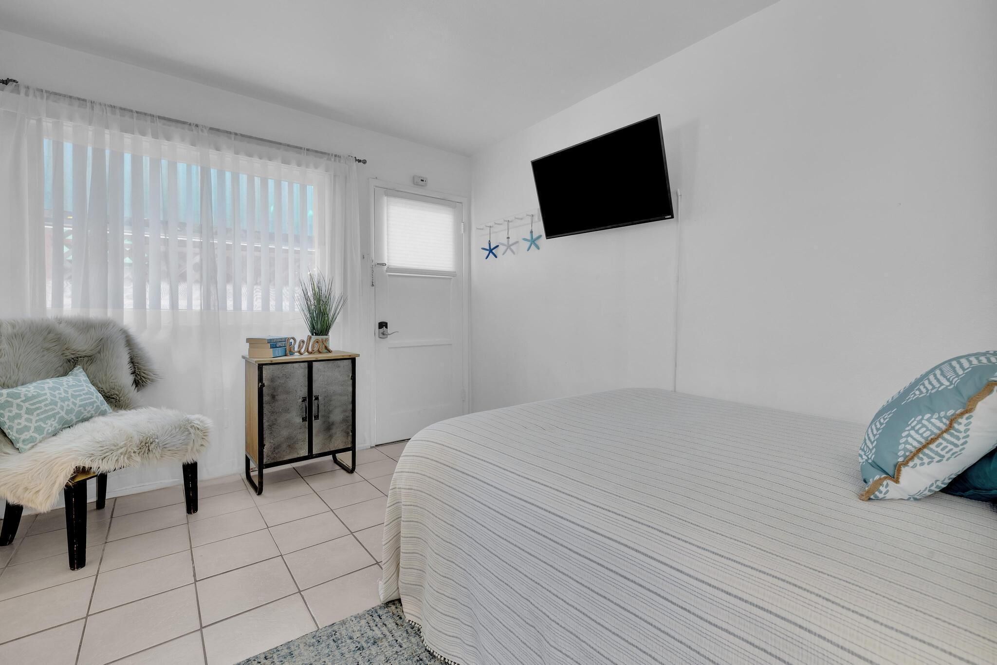 Une chambre avec un lit, une chaise, une petite armoire et un téléviseur fixé au mur.