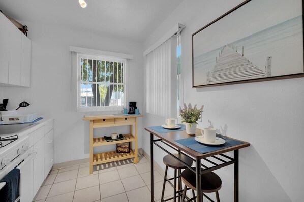 A compact kitchen with white cabinets, a wooden table, and a window with blinds.