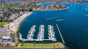 An aerial view of a marina with boats docked, a beach area with umbrellas, and a cityscape in the background. - #4286 PB Studio Walk to BAY, PIER & BEACH 🏝 (San Diego)