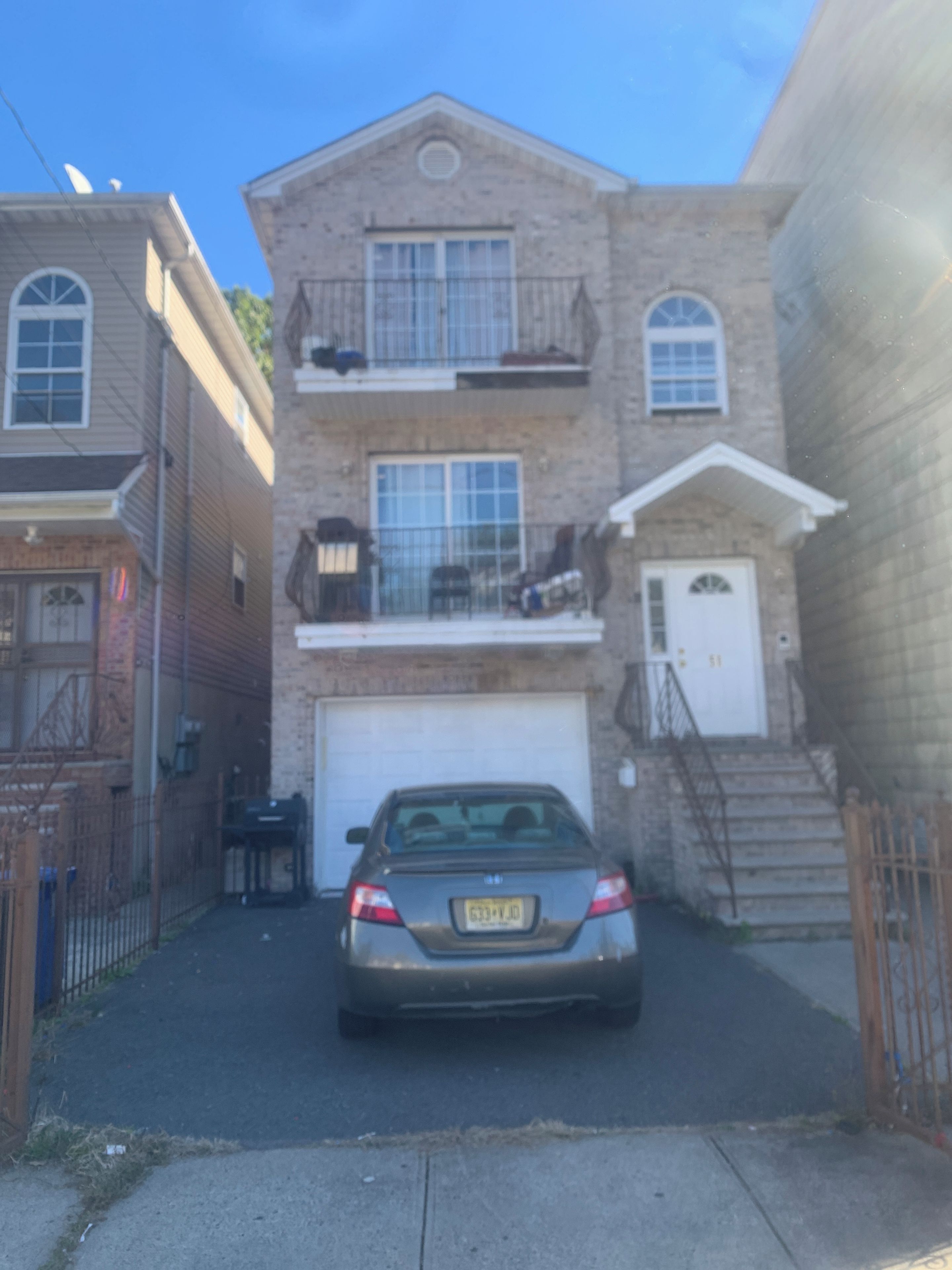 Un bâtiment à deux étages, avec un garage, une voiture garée et un escalier menant à l’entrée.