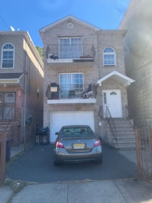 Un bâtiment à deux étages, avec un garage, une voiture garée et un escalier menant à l’entrée.