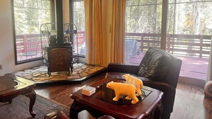 A cozy room with a fireplace, a leather chair, a coffee table with a polar bear figurine, and large windows with curtains. - ManVee Lodge at Yosemite - Just 2 miles from the south gate entrance to Yosemite (fish camp)