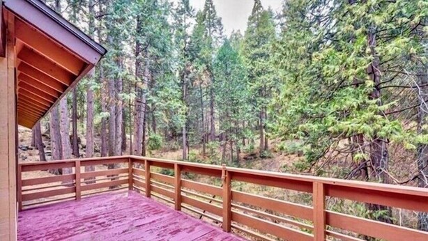 A wooden deck with a red floor, surrounded by a forest with tall trees. - ManVee Lodge at Yosemite - Just 2 miles from the south gate entrance to Yosemite (fish camp)