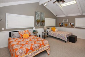 Une chambre avec deux lits, un ventilateur de plafond et une grande fenêtre avec des stores.