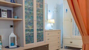 A bedroom with a wooden dresser, a mirror, and a bedside table with a lamp. - Cosmopoli - Sogni di Mare (Portoferraio)