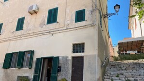 A building with green shutters, a black door, and a staircase leading up to a theater. - Cosmopoli - Sogni di Mare (Portoferraio)