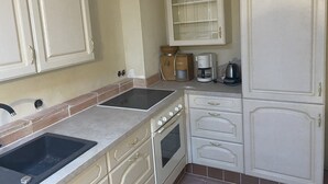 A kitchen with white cabinets, a sink, a stove, and a coffee maker. - The Finca - Your vacation in the Spanish Rhön (Hünfeld)