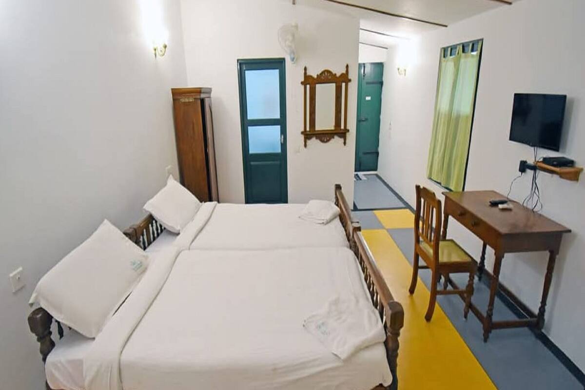 A room with two beds, a desk, a chair, a TV, and a wardrobe.