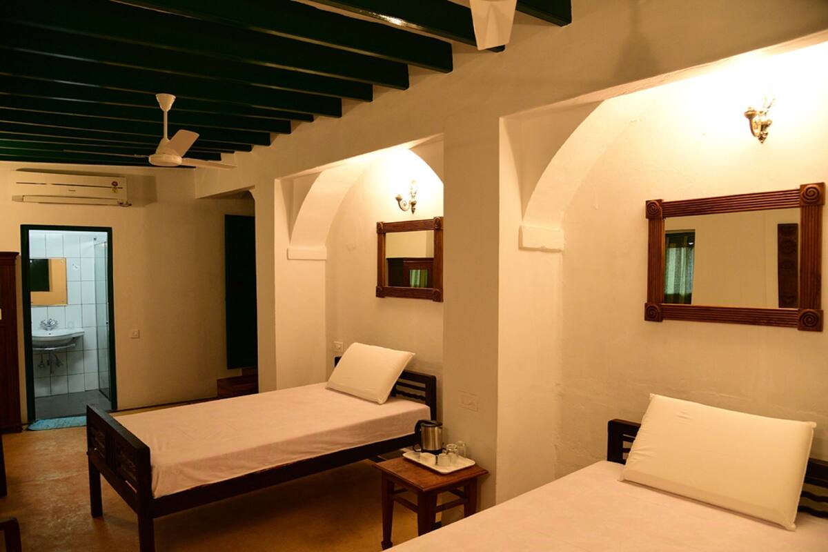 A hotel room with two beds, a small table, a mirror, and a ceiling fan.