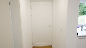 A narrow hallway with wooden flooring, white walls, and a white door at the end.