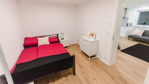 A bedroom with a bed, bedside tables, a dresser, and a view into the kitchen.