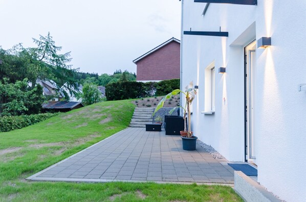 A modern house with a paved driveway, a potted plant, and a solar panel on the roof.