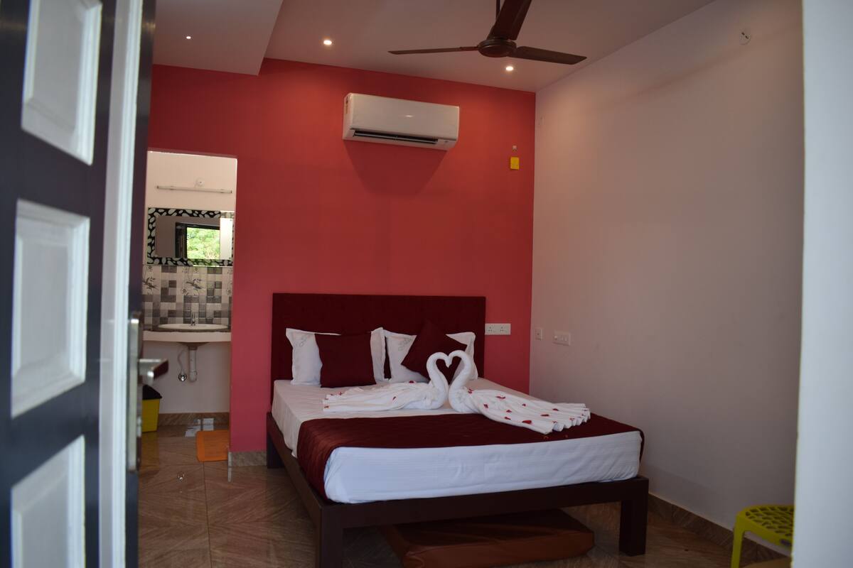 A bedroom with a red accent wall, a bed with white linens, a ceiling fan, and an air conditioning unit.