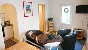 Un espace de vie compact comprenant un coin cuisine, un coin repas avec une table et des chaises, un téléviseur et une porte décorée d’une guirlande.